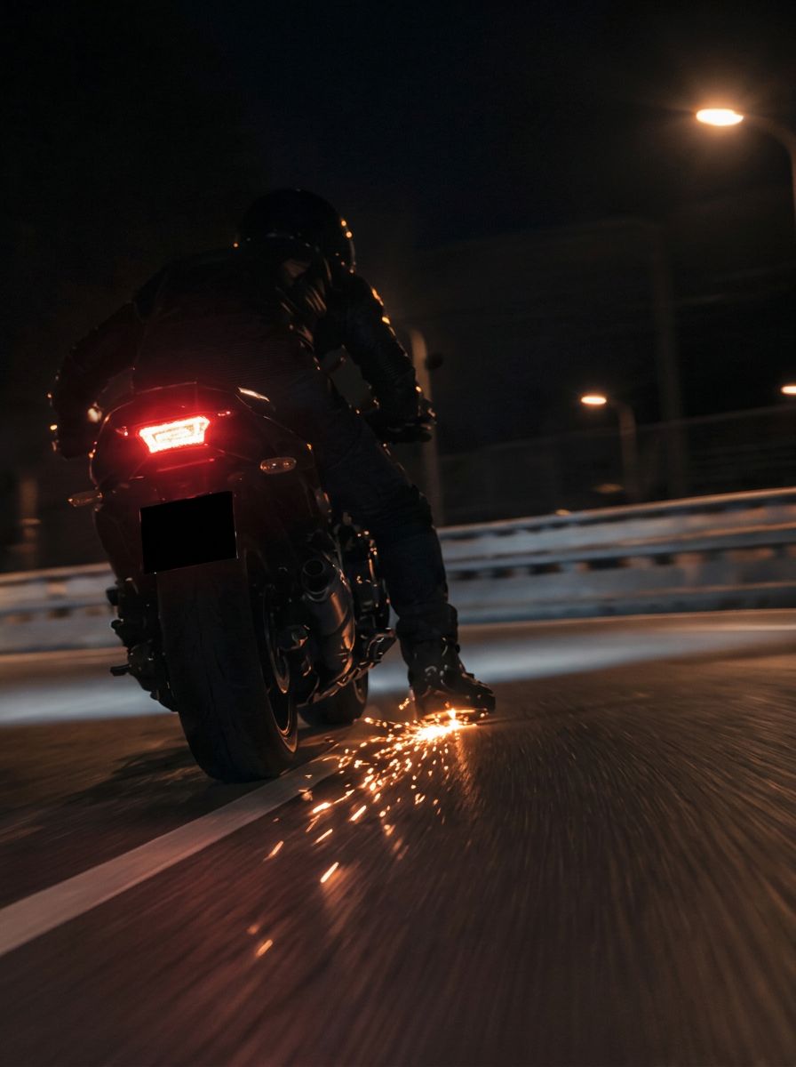 Motorcyclist riding low at night as sparks stream from under the rider's foot along the road